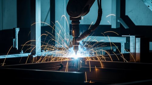 Ein Industrieroboter beim Schweißen von Metallteilen, umgeben von hellen Funken in einer modernen Produktionsumgebung.